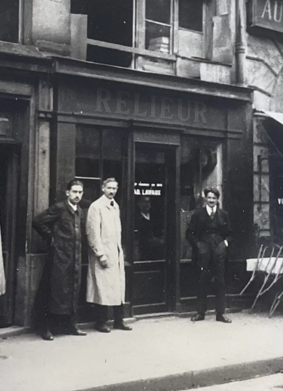 Relieur d’art devant l’ancienne échoppe de son atelier place Dauphine, Paris, photo d’époque illustrant une tradition artisanale de reliure dorure